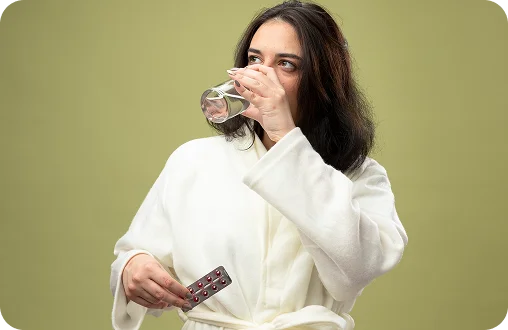 A woman in a white robe drinking a glass of water